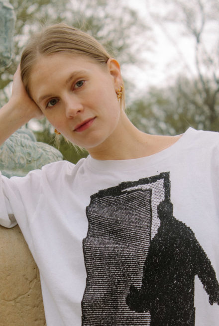 Emma Holten med hovedet på skrå i hvid t-shirt og sorte bukser i park