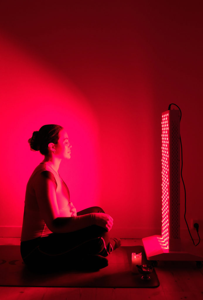 Gravid kvinde i lotusstilling foran red-light therapy lampe