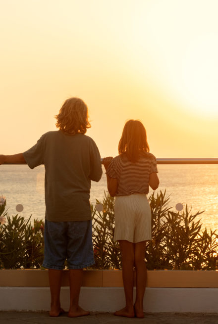 to børn på ferie i varmen, står og kigger på solnedgang udover havet